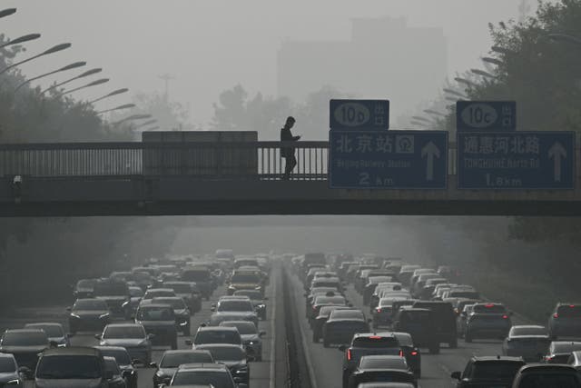 <p>Pedestrians walk on an overpass as traffic snarls amid haze from air pollution in Beijing in 2023</p>