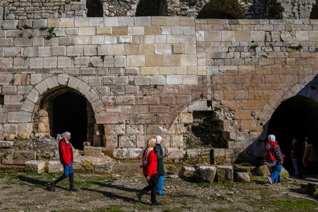 <p>People walk past a damaged section of Krak des Chevaliers, whcih caused by the Assad regime shilling in 2014</p>